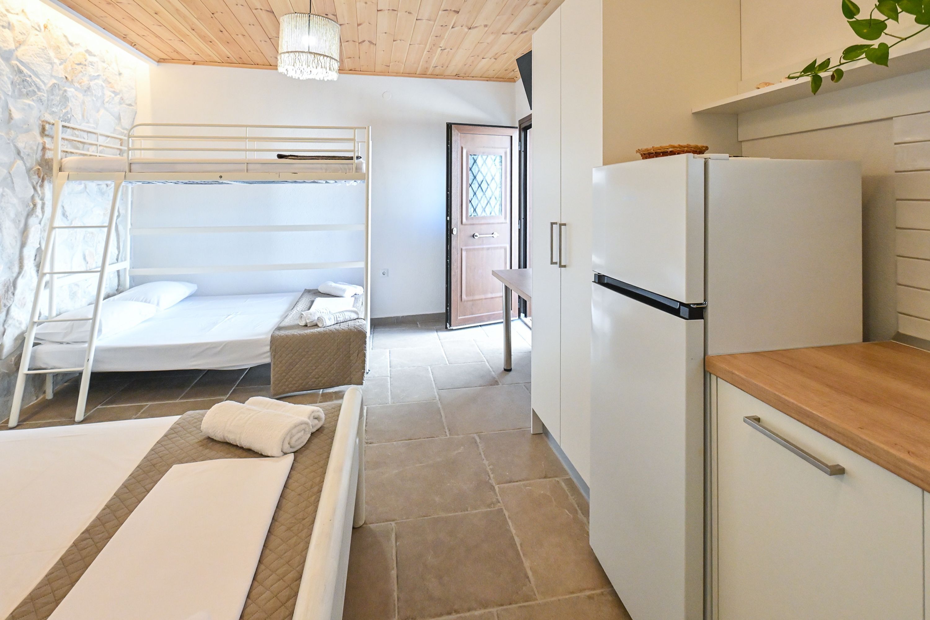A bunk bed with a ladder, a small table with a towel, a refrigerator, and a kitchen area with cabinets.