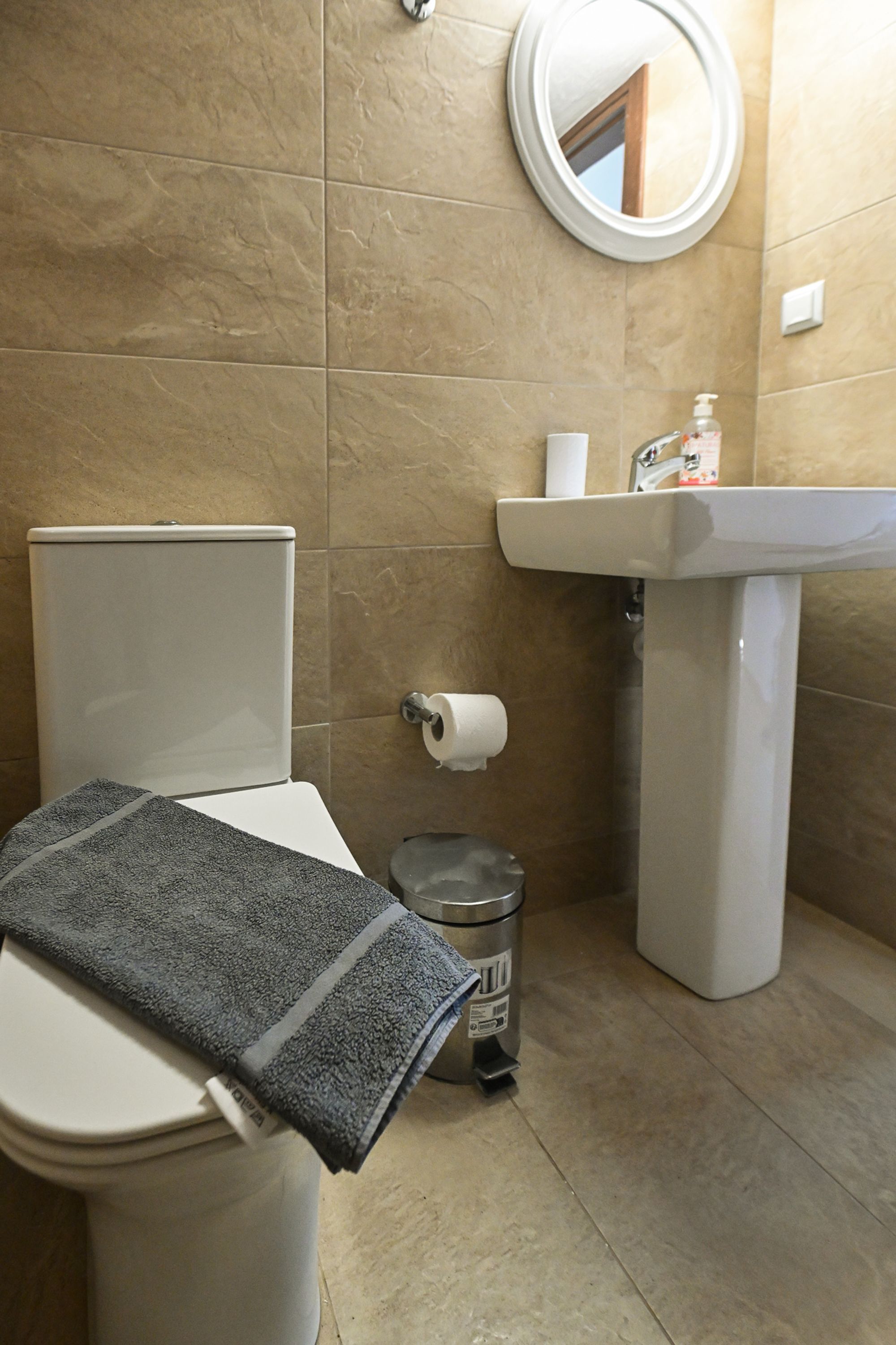 A bathroom with a toilet, a sink, a mirror, and a trash bin.
