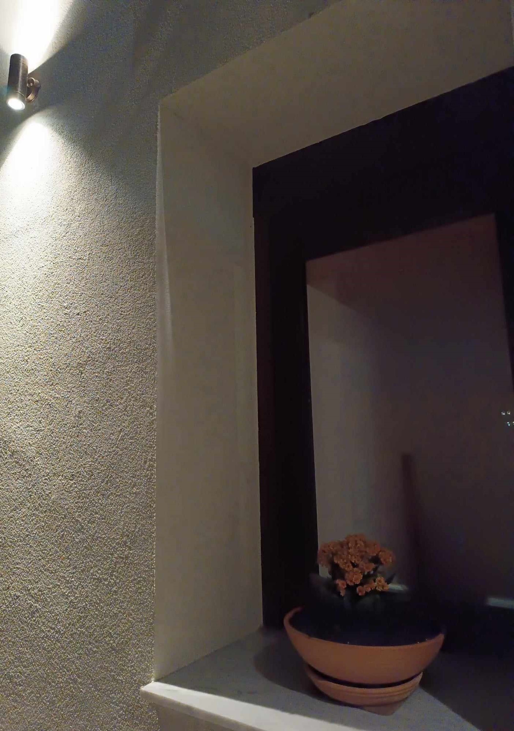 A corner with a textured wall, a dark-framed mirror, and a terracotta bowl with a plant.