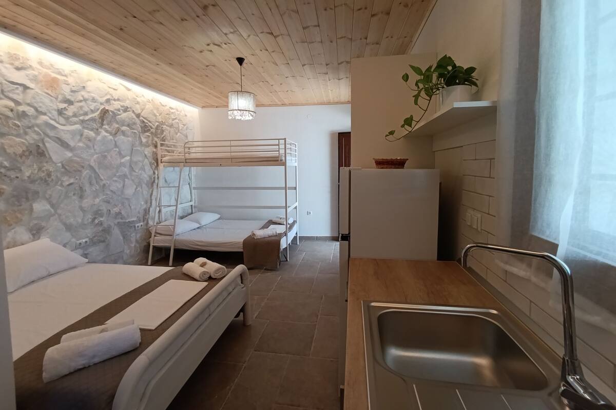 Una habitación de hotel compacta con literas, kitchenette, pared de piedra y lámpara colgante.