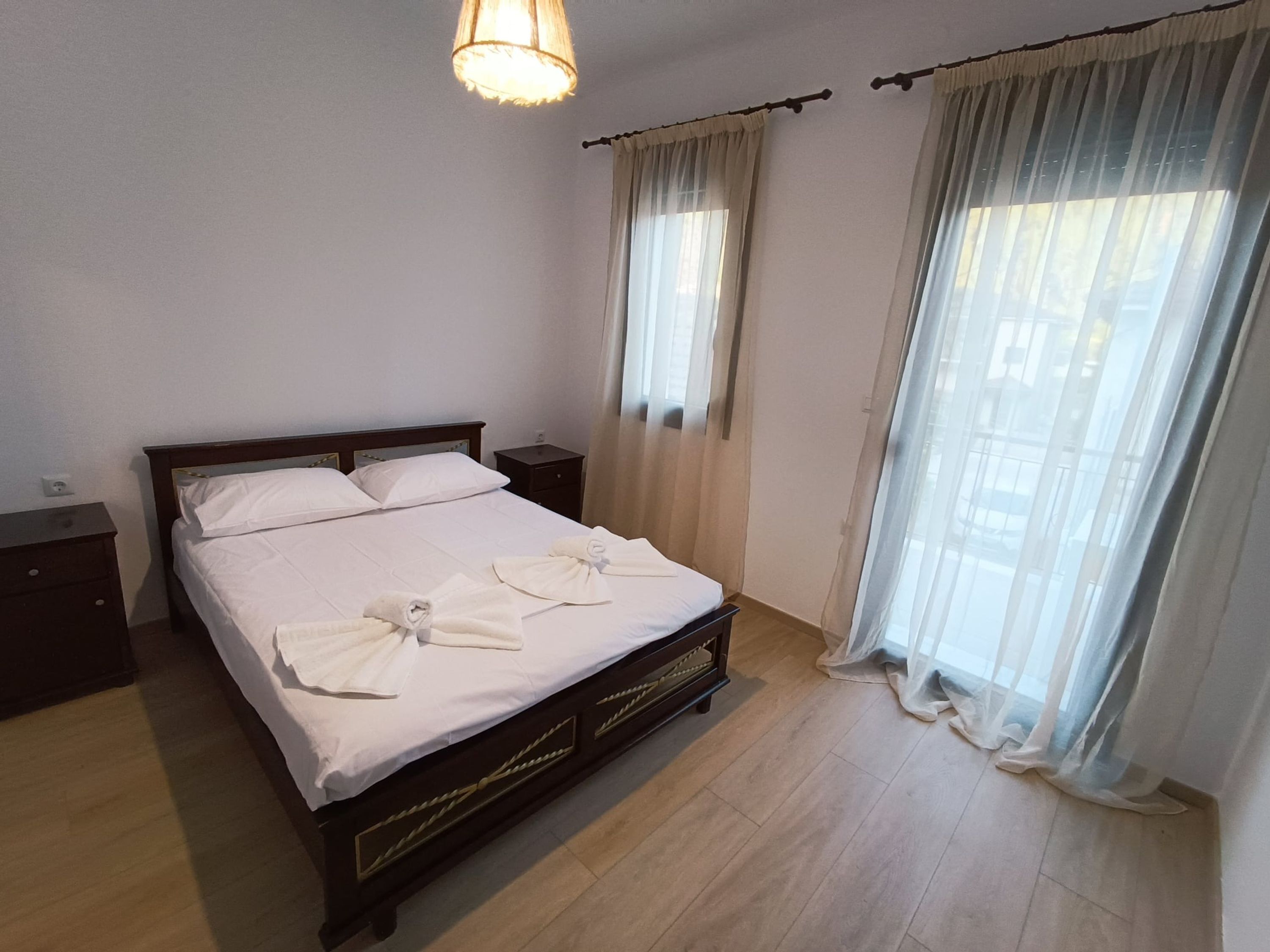 A neatly made bed with white linens and towels, a wooden headboard, and a bedside table with a lamp.
