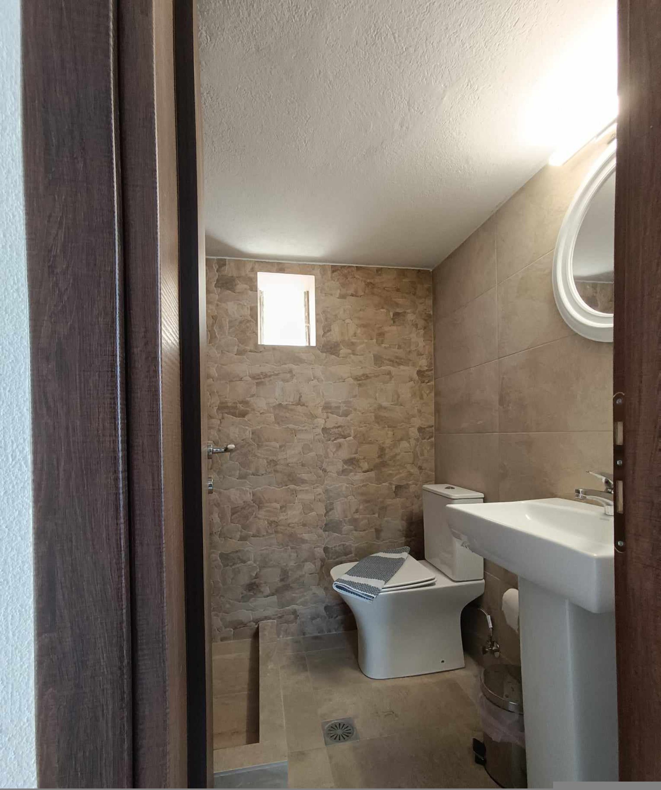 A bathroom with a stone wall, a toilet, a sink, and a small window.