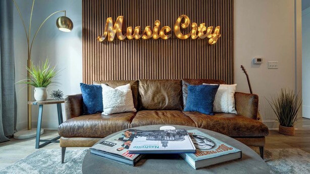 Una sala de estar moderna con un sofá de cuero, una mesa de centro con revistas, una lámpara de pared que dice "Music City" y un panel de madera vertical.