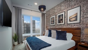 Una habitación de hotel moderna con una cama grande, pared de ladrillo y cuadros enmarcados.
