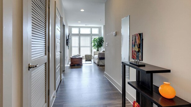 A hallway with a dark wood floor, a black console table with a vase, and a door with horizontal slats. - Quiet Condo l Prime Locale & mins to DT (Nashville)