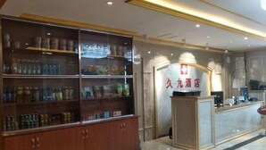 A hotel reception area with a reception desk, a display of bottled water, and a wooden cabinet with various items.