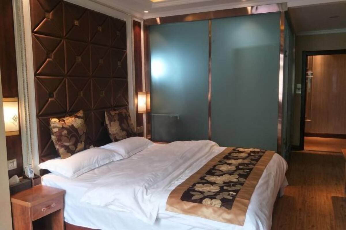 Een hotelkamer met een bed, een houten nachtkastje, een muur met een geometrisch patroon, en een deur.