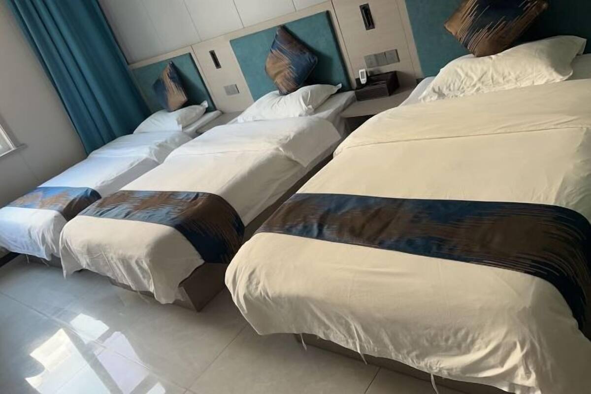 Een hotelkamer met vier bedden op een rij, elk voorzien van witte lakens en een gestreept plaid.