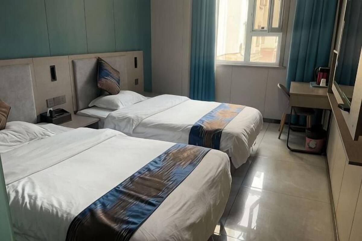 Een hotelkamer met twee bedden, een bureau, een stoel, een raam met gordijnen en een klein tafeltje.