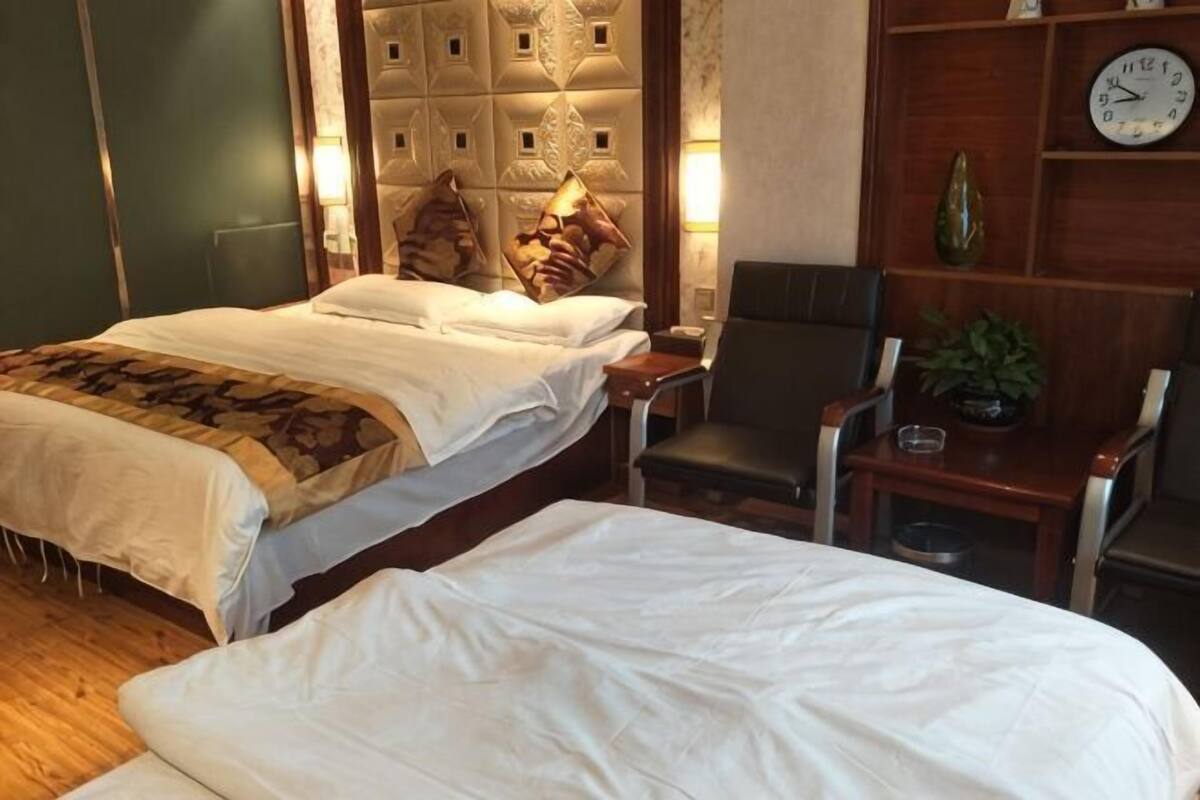 Een hotelkamer met twee bedden, een houten hoofdeinde, een klok en een klein tafeltje met een plant.