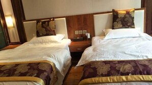 A hotel room with two beds, each with a floral-patterned bedspread and matching pillows. There is a wooden headboard and a nightstand with a lamp.