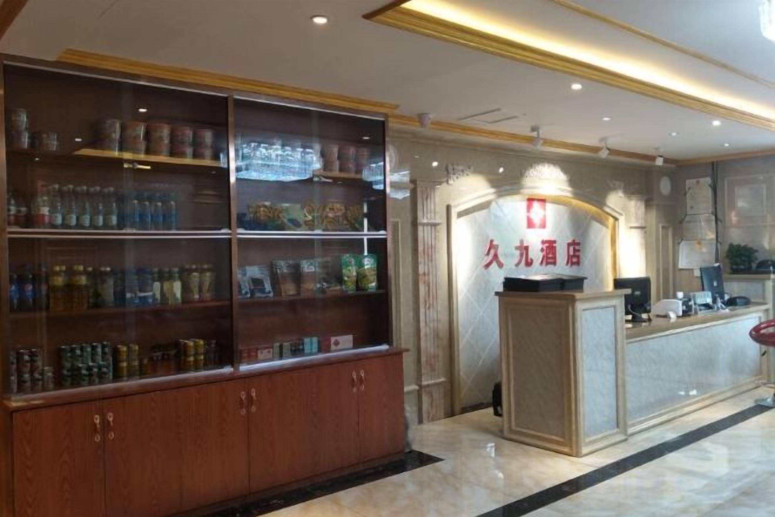 A hotel reception area with a glass display case filled with various items, a reception desk with a sign, and a marble floor.