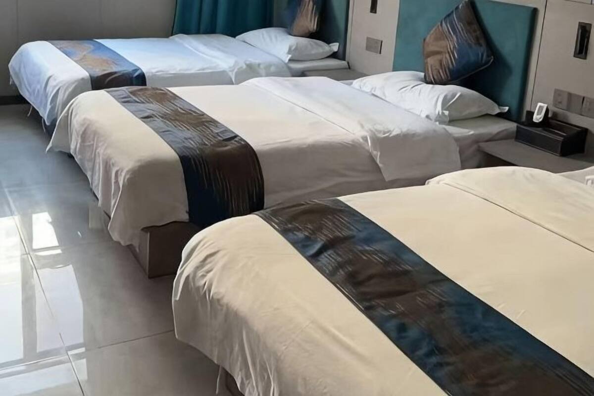 Drie bedden met wit en blauw beddengoed, een nachtkastje met een telefoon en een nachtlampje.