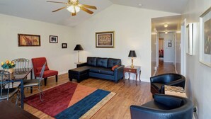 Un salón amplio con un sofá de múltiples plazas, un sillón rojo, un sillón azul, piso de madera y un ventilador de techo.