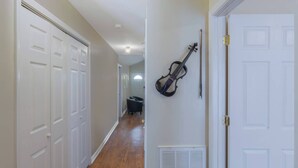 Un pasillo con puertas blancas, un violín en la pared y una rejilla de ventilación cerca de la puerta.