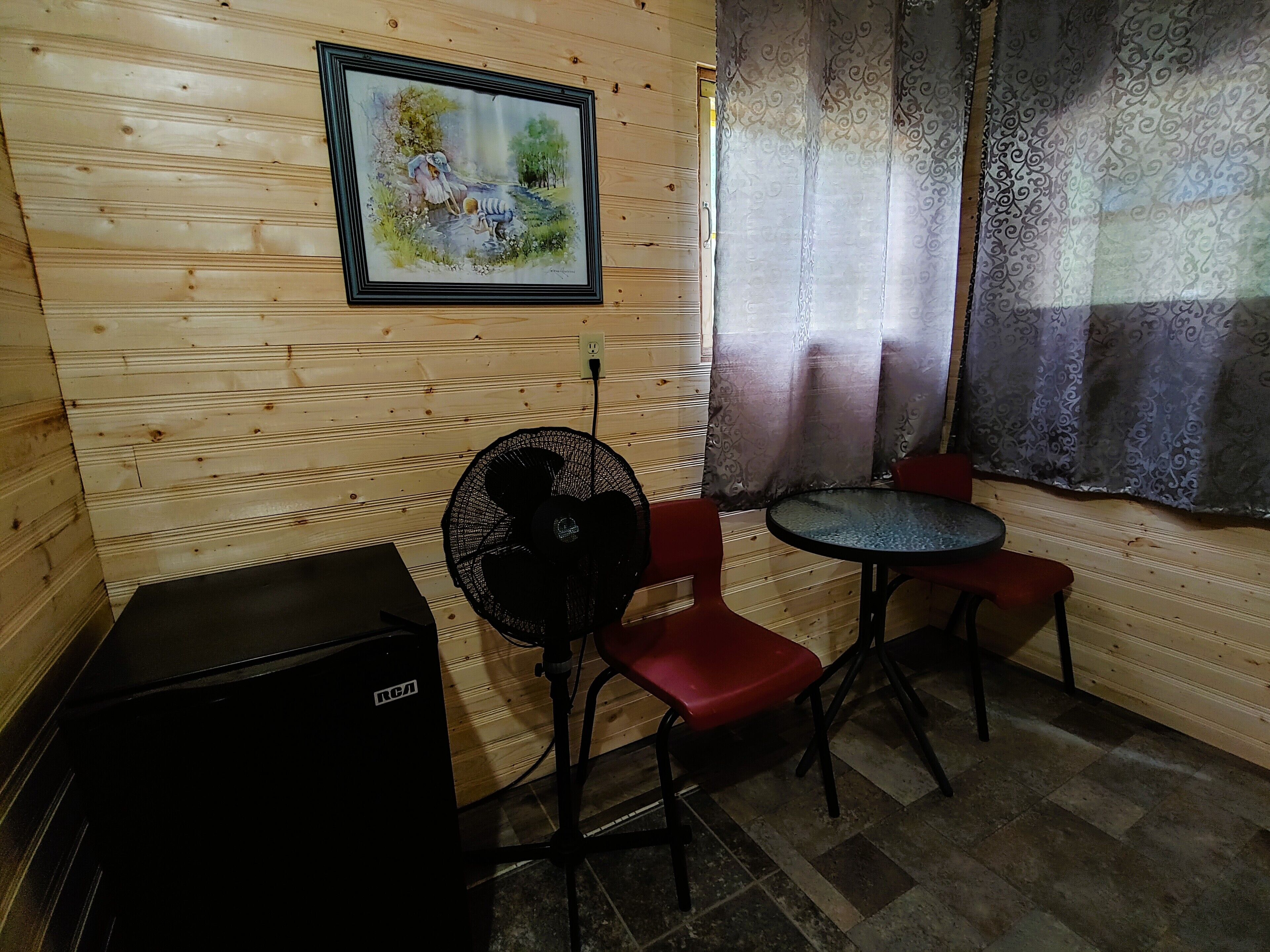 A wooden room with a painting, a fan, a table, and two chairs.