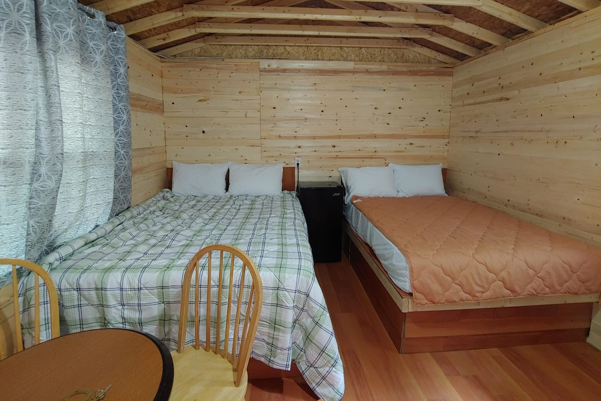 Une petite pièce agréable et chaleureuse, avec deux lits, un plafond en bois et une table entourée de chaises.