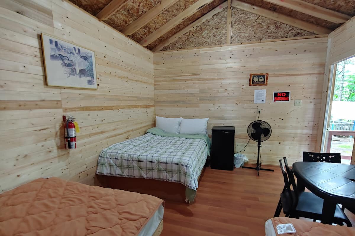 Une cabane en bois comprenant deux lits, une table, un ventilateur, un extincteur et un panneau indiquant «Il est interdit de fumer».