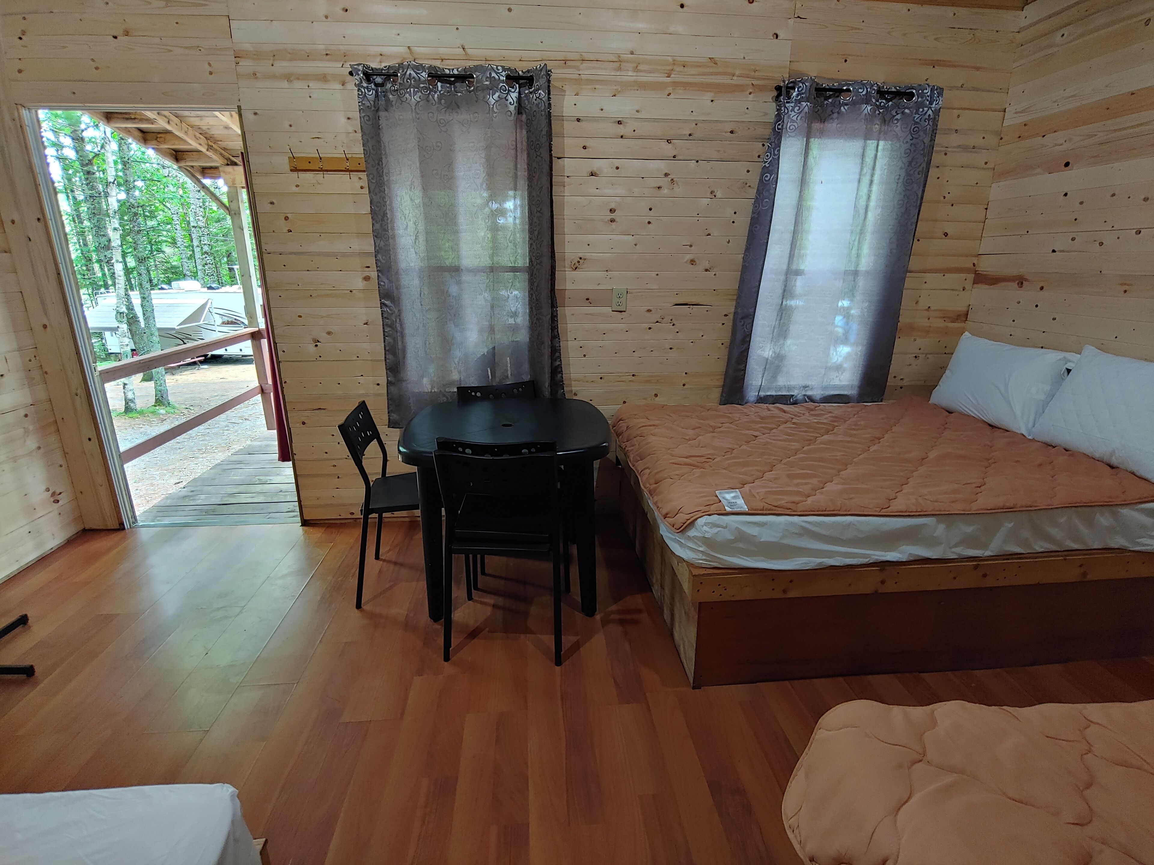 Una habitación de cabaña de madera con una cama, una mesa con sillas y un ventanal con cortinas.