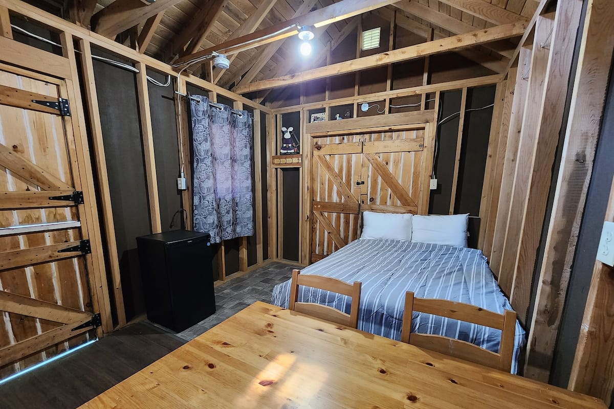 Une pièce rustique en bois, avec un lit, une table et un haut-parleur noir.
