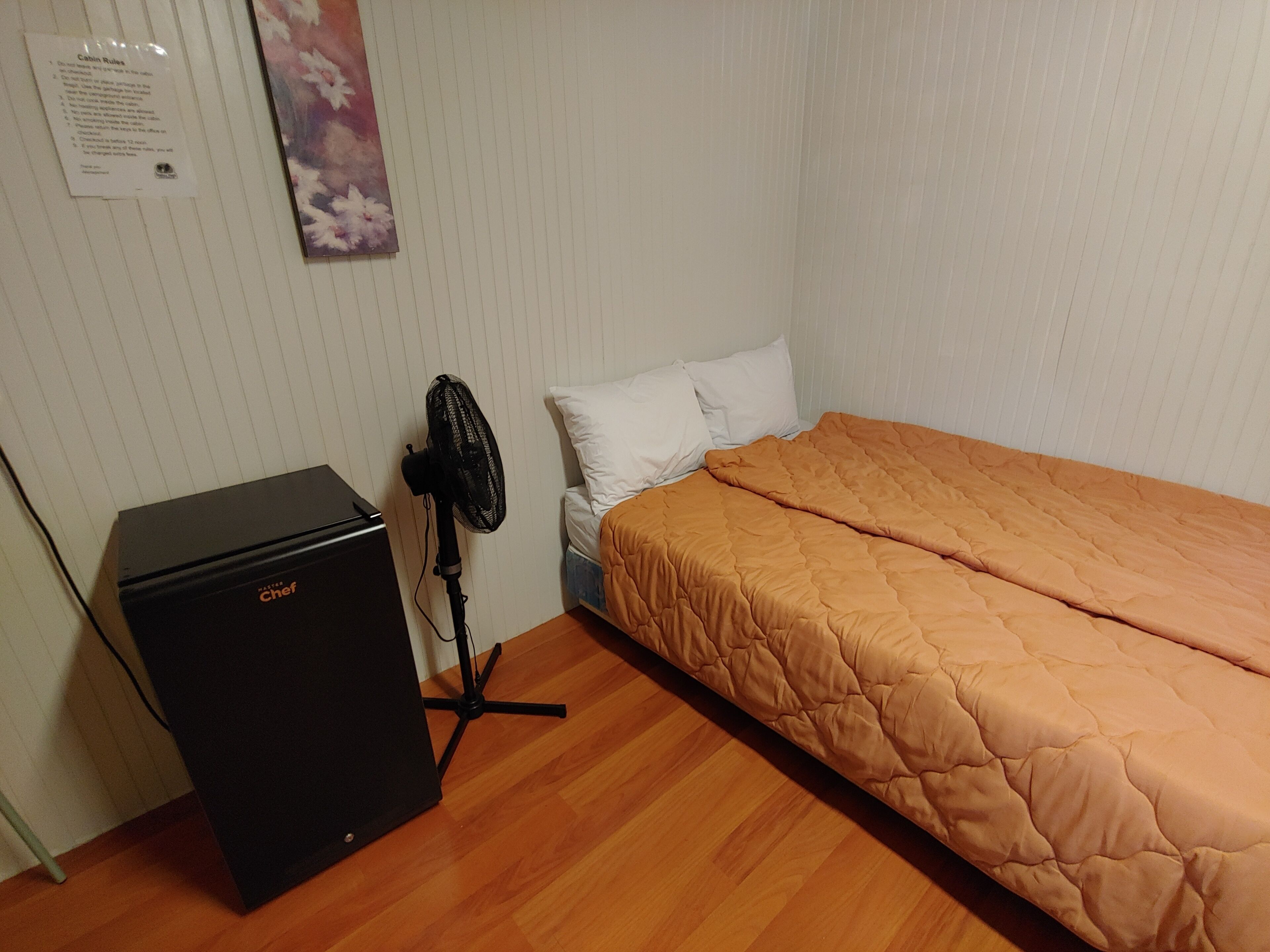 Ein kleines Zimmer mit einem Bett, einem Heizgerät und einem Ventilator.