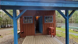Une cabane en bois dotée d’une véranda, de deux fenêtres et d’une porte donnant sur l’intérieur.