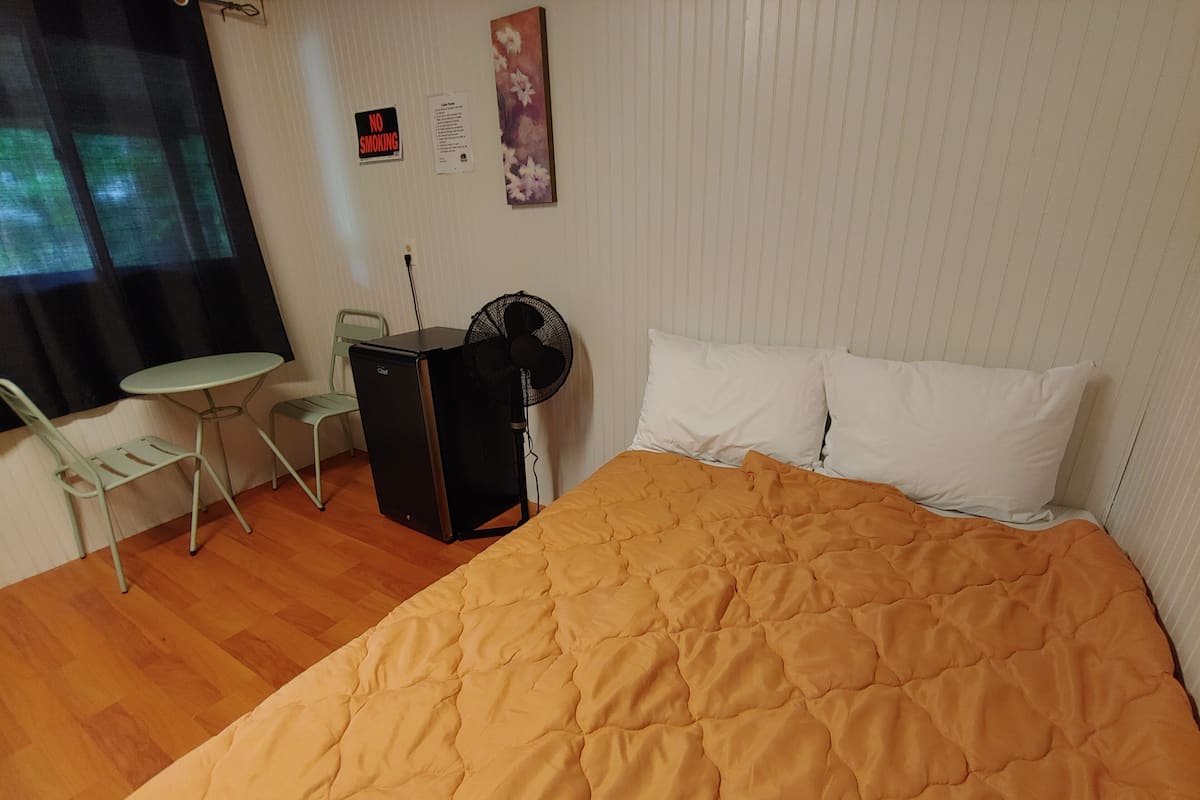 Une chambre d’hôtel équipée d’un lit, d’un bureau, d’une chaise, d’un ventilateur et d’une fenêtre avec des rideaux.