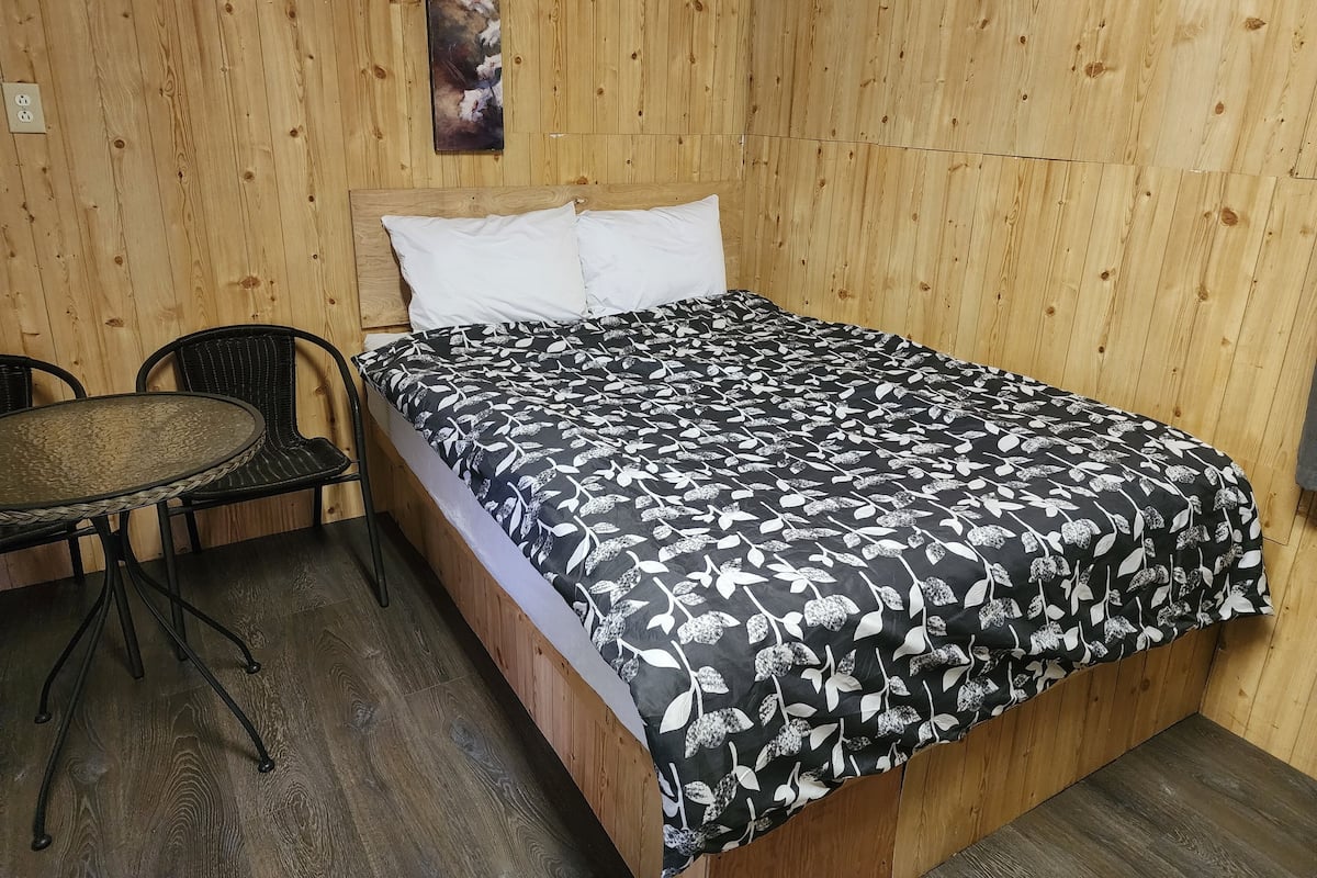 Une pièce aux murs lambrissés, avec un lit, une table ronde et une chaise.