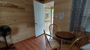 L’intérieur d’une cabane en bois comprend un coin repas, un ventilateur et une porte donnant sur l’extérieur.