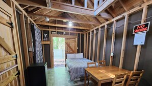 Une pièce rustique en bois, avec un lit, une table et des chaises. Un panneau « Il est interdit de fumer » est affiché sur le mur.