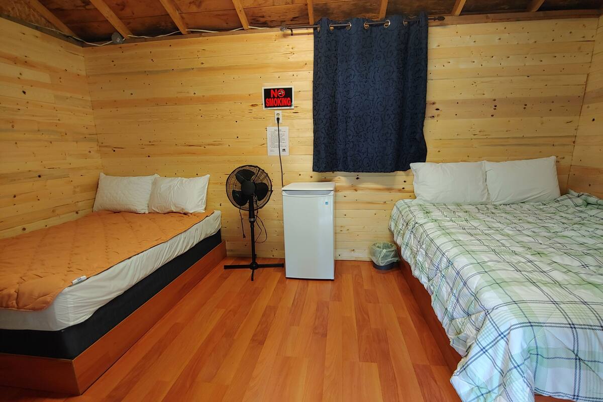 Une chambre de style cabane avec deux lits, un ventilateur, un petit réfrigérateur et un panneau indiquant qu'il est interdit de fumer.