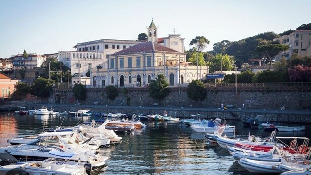 Una marina con imbarcazioni ormeggiate di fronte a un edificio storico con finestre ad arco e un campanile.