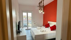 Una camera da letto con un letto, una scrivania e una sedia. Si vede una finestra che offre una vista sugli edifici.