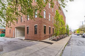 A multi-story brick building with a garage door, a sidewalk, and trees along the street.