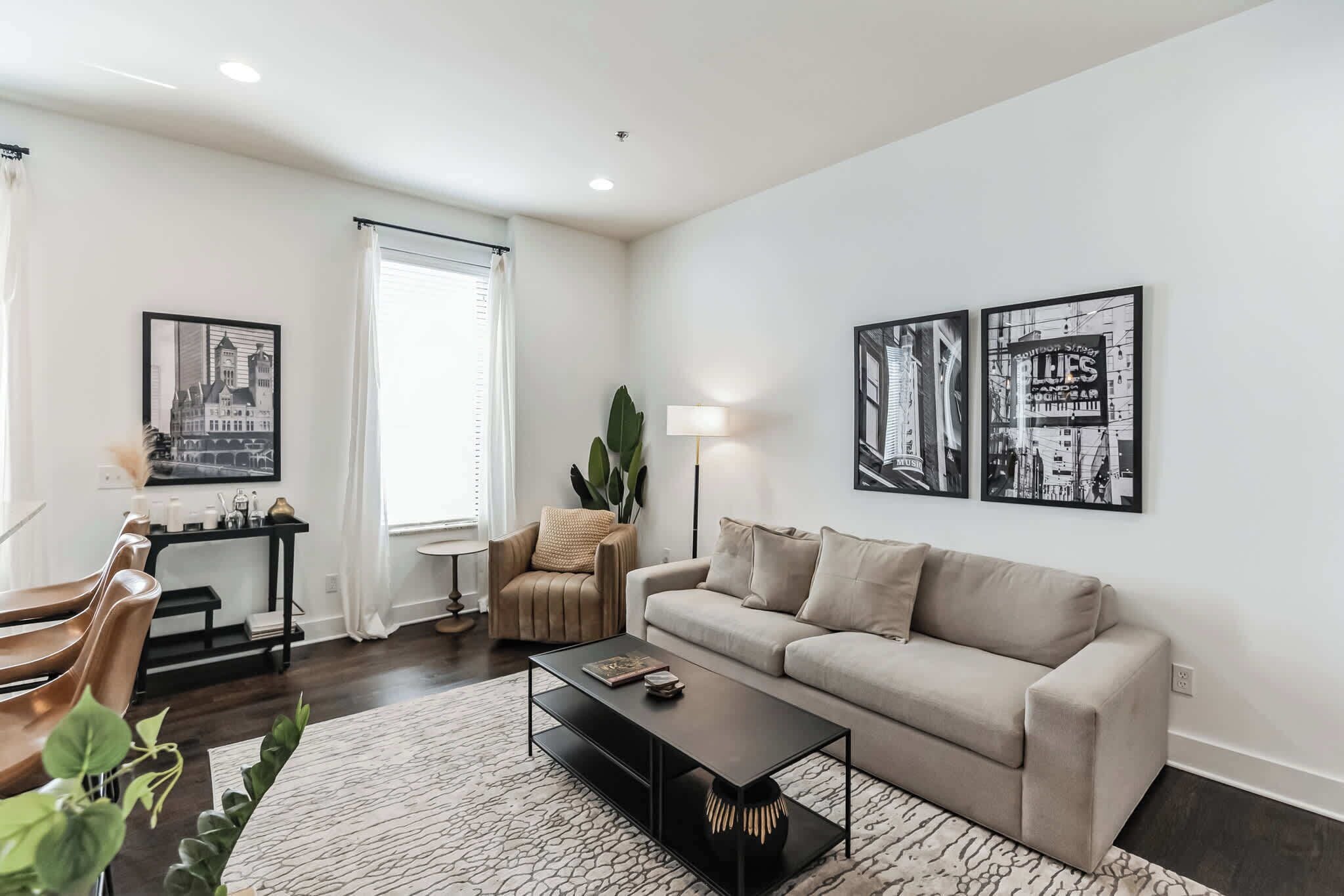 A modern living room with a sofa, coffee table, and chairs. There are framed pictures on the wall, a lamp, and a plant.