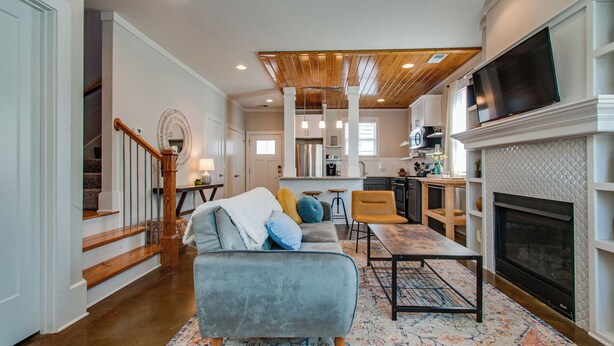 A spacious living area with a fireplace, a dining table, and a kitchen in the background. - Charming Home | Near DT, Pet Friendly! (Nashville)