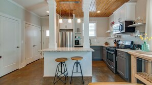 A modern kitchen with a wooden ceiling, white cabinets, a central island with stools, stainless steel appliances, and a microwave on the countertop. - Charming Home | Near DT, Pet Friendly! (Nashville)