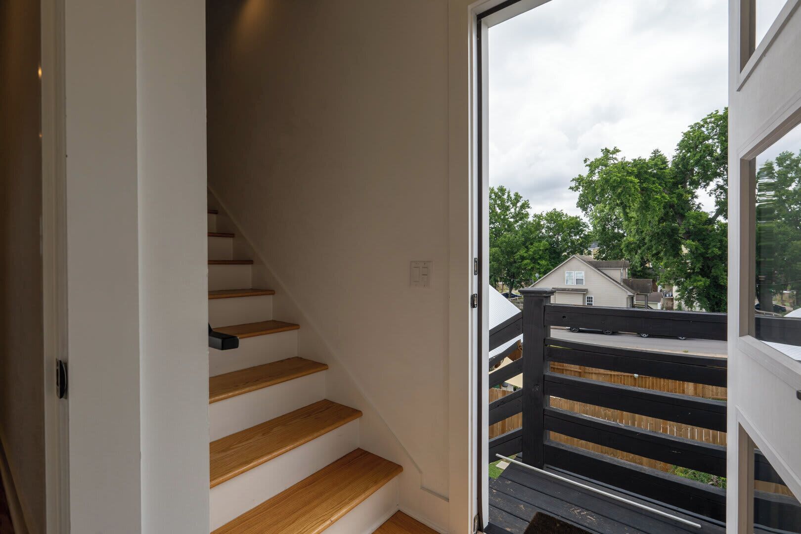 Een trap met houten treden die leidt naar een balkon met een zwarte leuning.