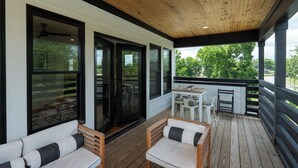 Un espace extérieur abrité doté d’une terrasse en bois, d’un coin salon avec un canapé et des fauteuils, ainsi que d’une table et de chaises.