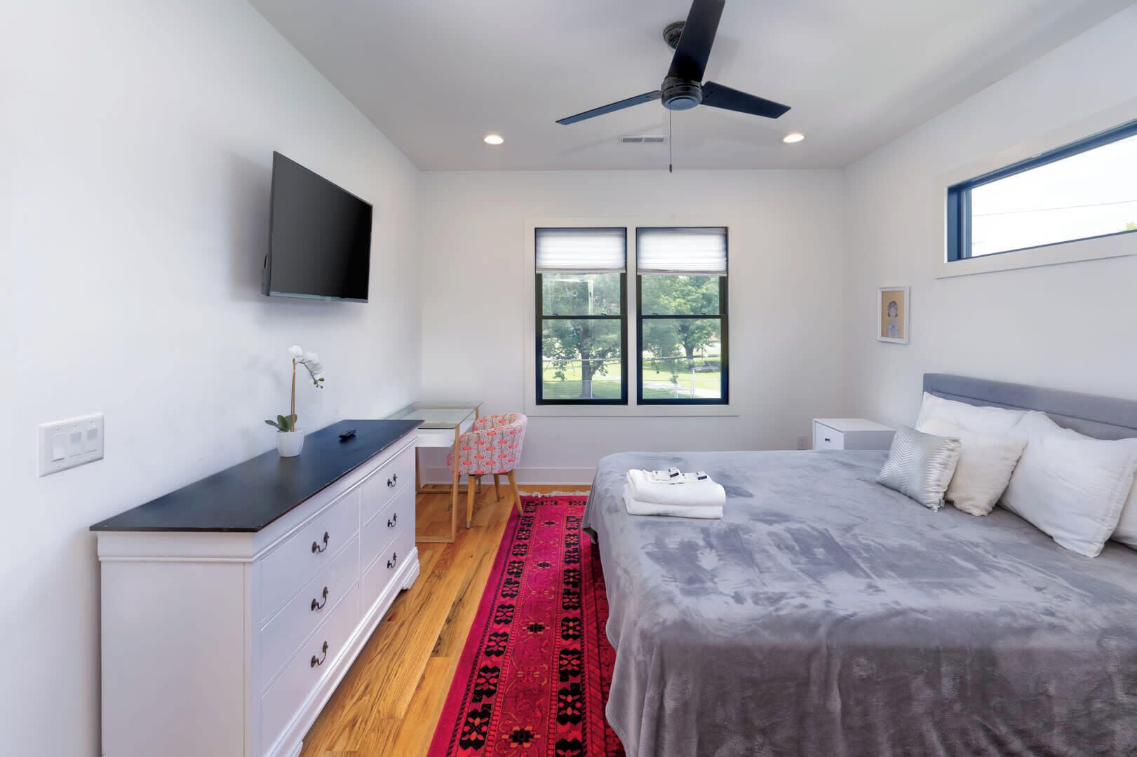 A bedroom with a bed, a desk, a chair, a TV, and a window with a view of trees.