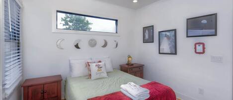Un dormitorio con cama, mesita de noche, ventana y adornos en la pared.