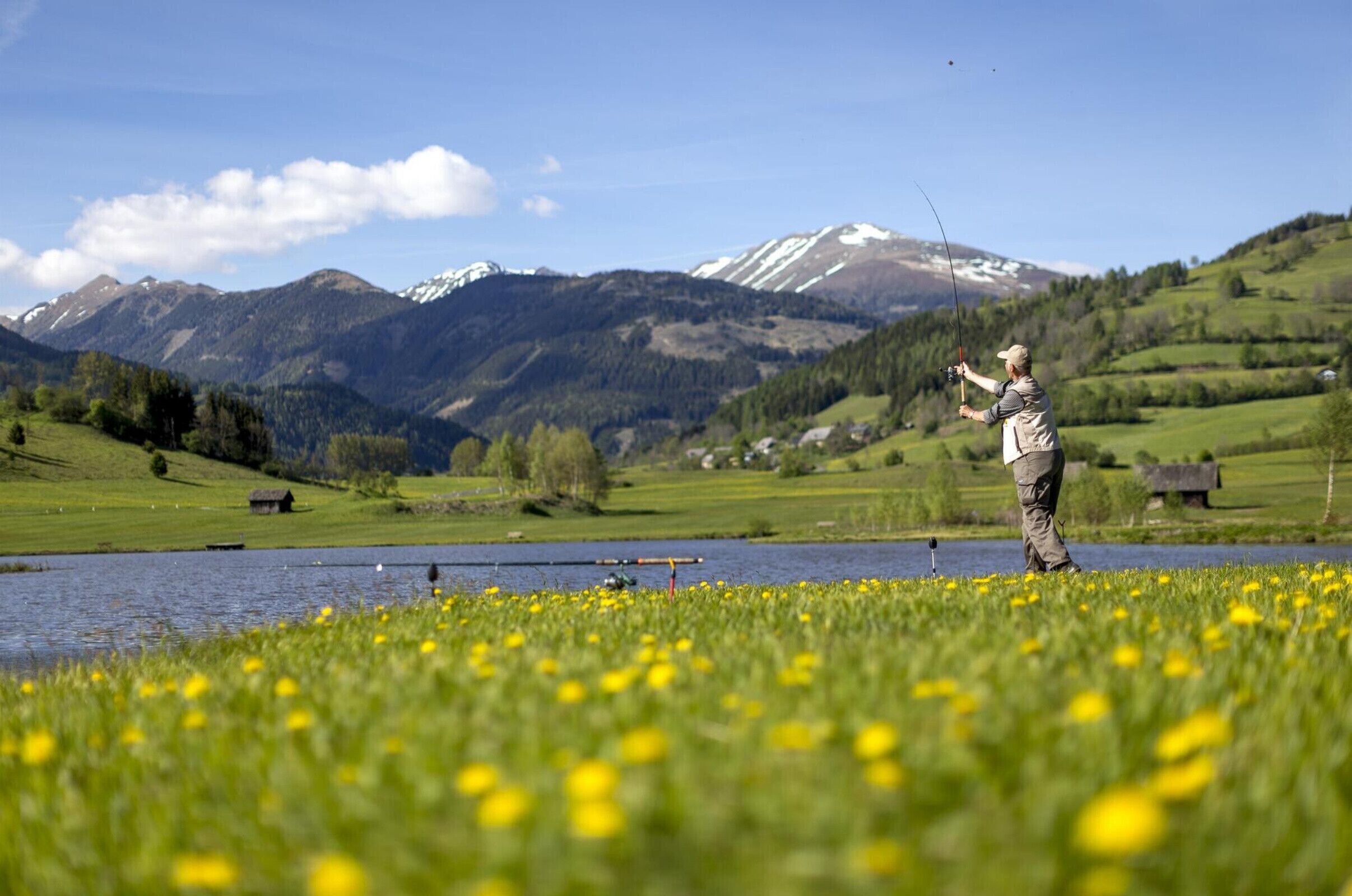 A person fishing by a lake with mountains in the background.