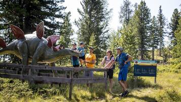 A group of people observing a dinosaur exhibit in a natural setting with a wooden fence and informational sign.