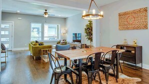 A modern dining area with a wooden table and chairs, a chandelier, and a large window providing natural light.