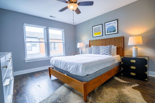 Une chambre à coucher comprenant un lit, deux lampes de chevet, un ventilateur de plafond, une fenêtre et une commode.