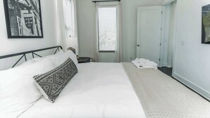 A bedroom with a large bed, a nightstand, a window with blinds, and a door. - Couple's Retreat Near Vanderbilt University! (Nashville)