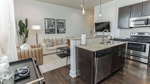 A modern kitchen with a central island, stainless steel appliances, and a dining area with a sofa and table. - Couple's Retreat Near Vanderbilt University! (Nashville)