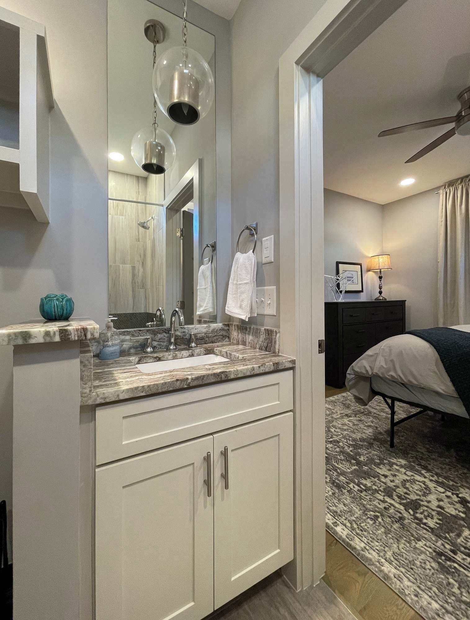Un baño moderno con encimera de mármol, un espejo grande y un ventilador de techo.
