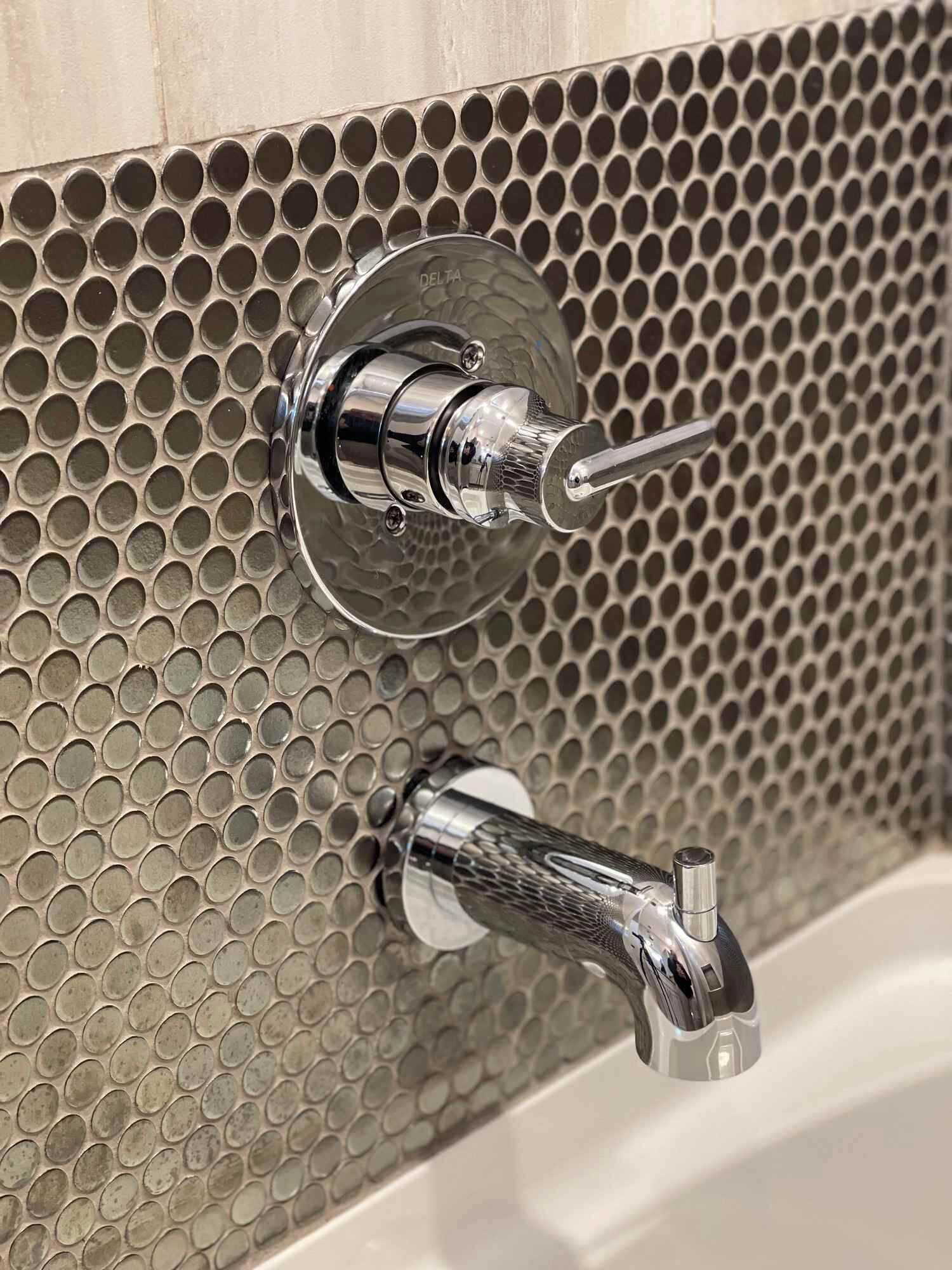 Een badkamer met een wand van geperforeerd metaal en twee chroomkleurige accessoires.