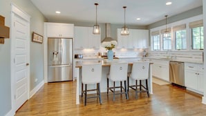 A modern kitchen with white cabinets, stainless steel appliances, and a central island with bar stools. - Private Backyard | Near Bicentennial Park (Nashville)